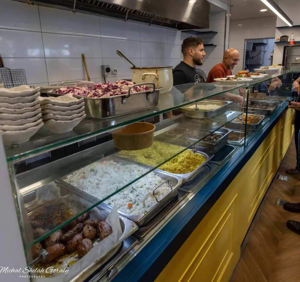 דוכן האוכל של המסעדה עם מגשי אורז, קוסקוס ותפוחי אדמה, והצוות מאחורי הדלפק