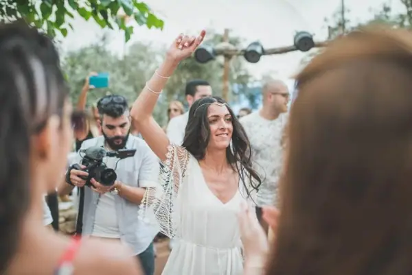 הכלה מרימה ידיים בשמחה בין המצלמים