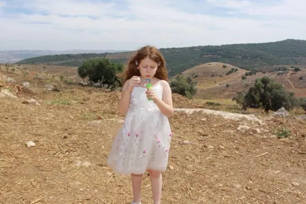 ילדה בשמלה לבנה בשדה פתוח על רקע גבעות
